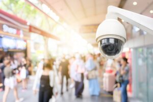 Modern public CCTV camera with blur crowd and shopping plaza background. Recording cameras for monitoring all day and night. Concept of surveillance and monitoring with copy space.