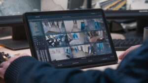 Male security officer controls CCTV cameras in office, uses digital tablet and computers with surveillance camera footage playback on screens. High tech security system. Monitoring and social safety.